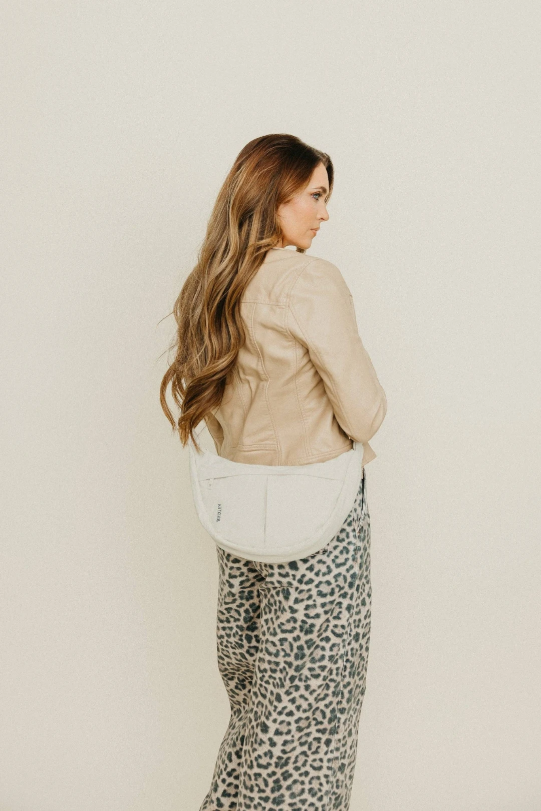 Woman wearing a beige jacket and leopard print pants against a plain background