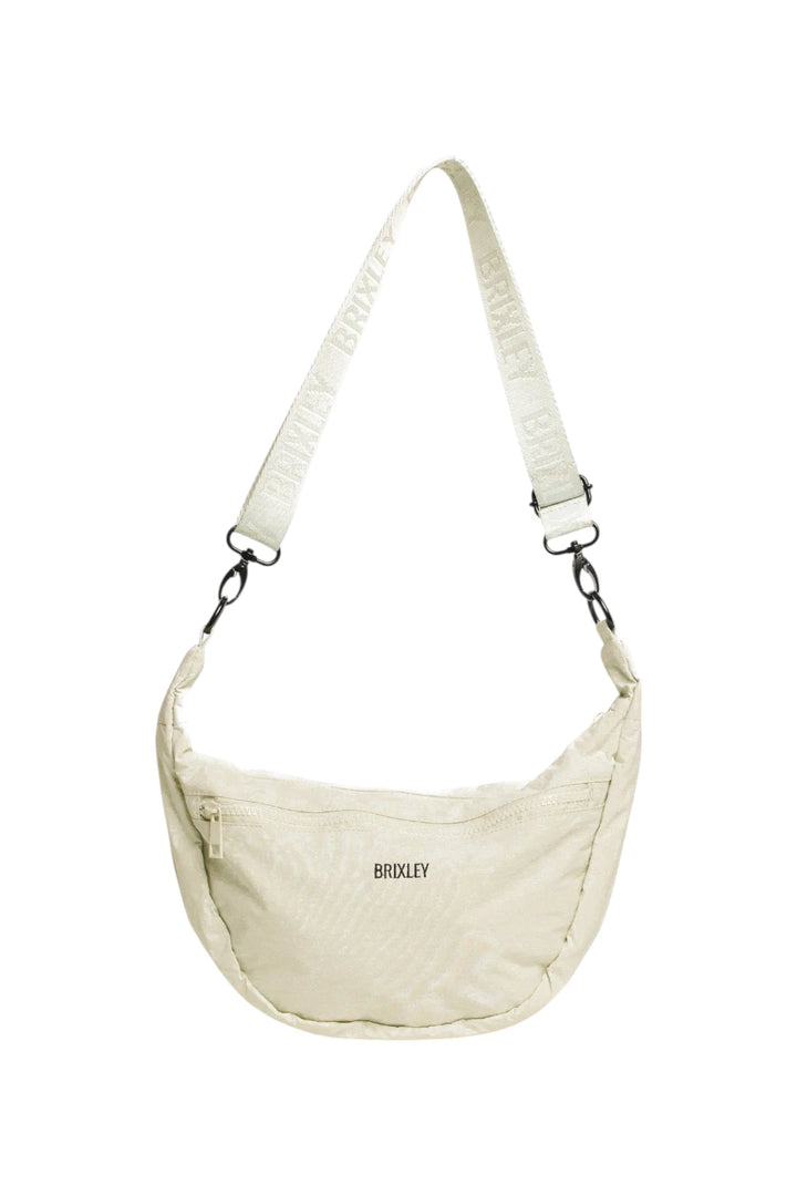 A cream-colored Brixley crescent-shaped crossbody bag with a matching branded shoulder strap, shown against a plain white background.