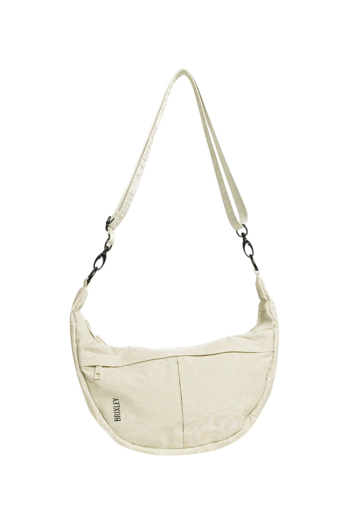 An off-white crescent-shaped shoulder bag with a matching adjustable shoulder strap, featuring a front zippered pocket and a small black 'BRIXLEY' logo, shown against a plain white background.