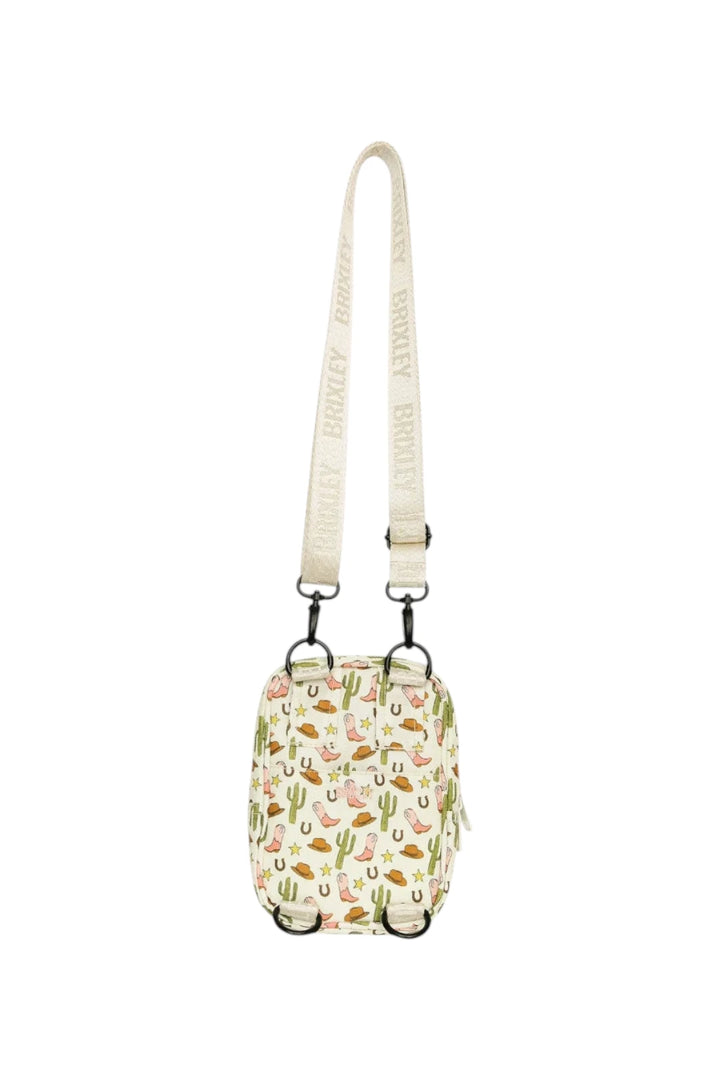 A small crossbody bag with a cream-colored strap and body, decorated with a colorful desert cactus and western pattern. The brand name 'BRIXLEY' is printed repeatedly on the strap.