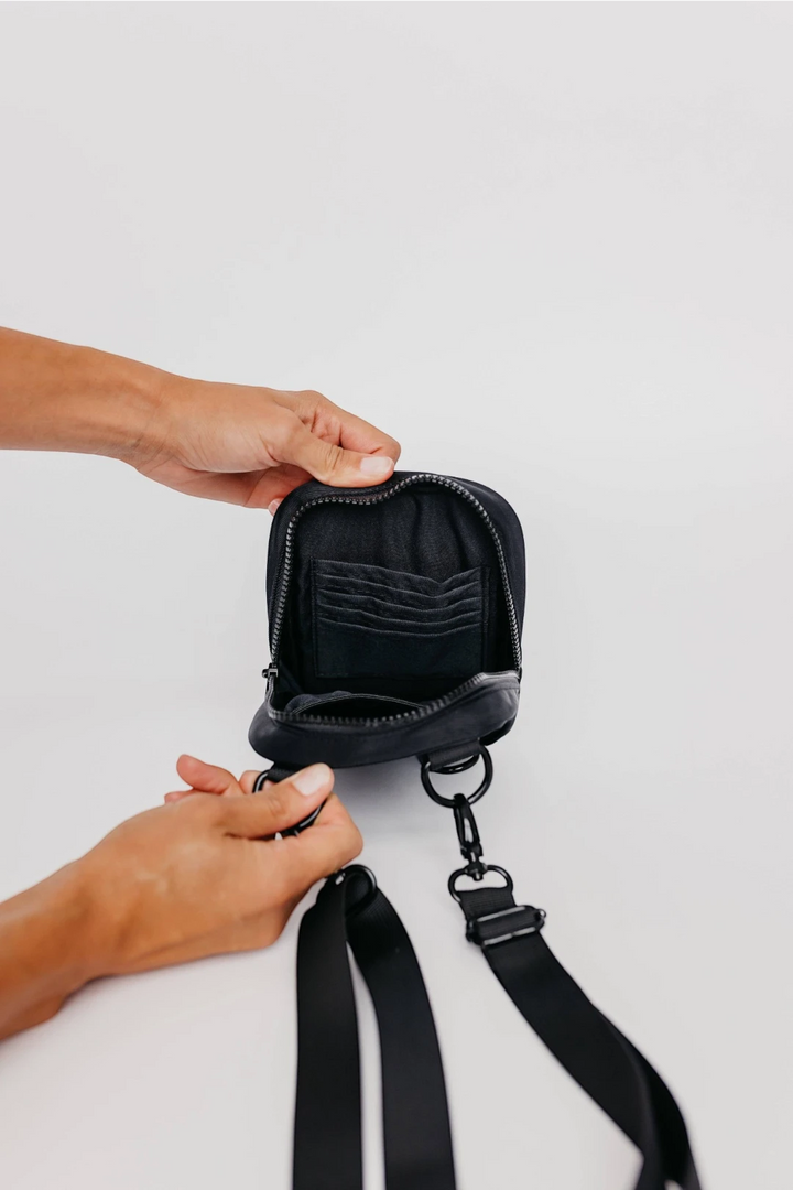 Person holding a black leather pouch with a strap on a light gray background