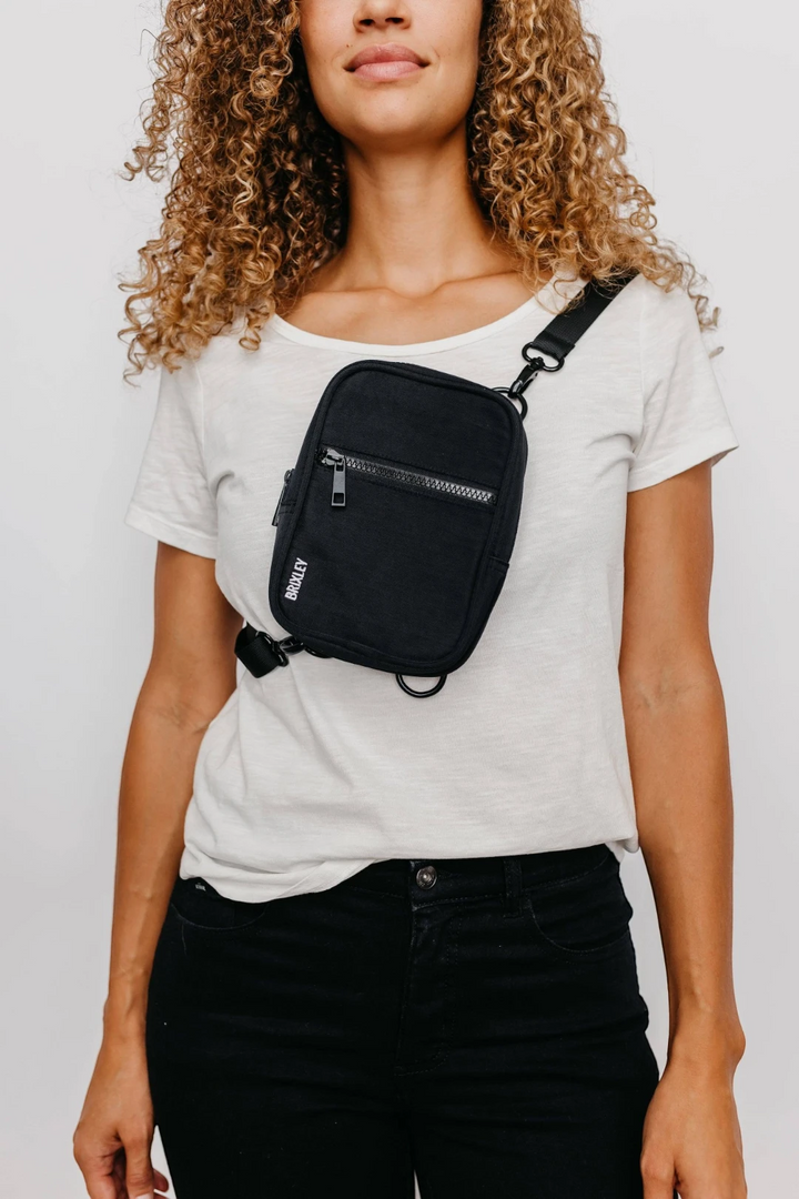 Person wearing a black crossbody bag on a plain background