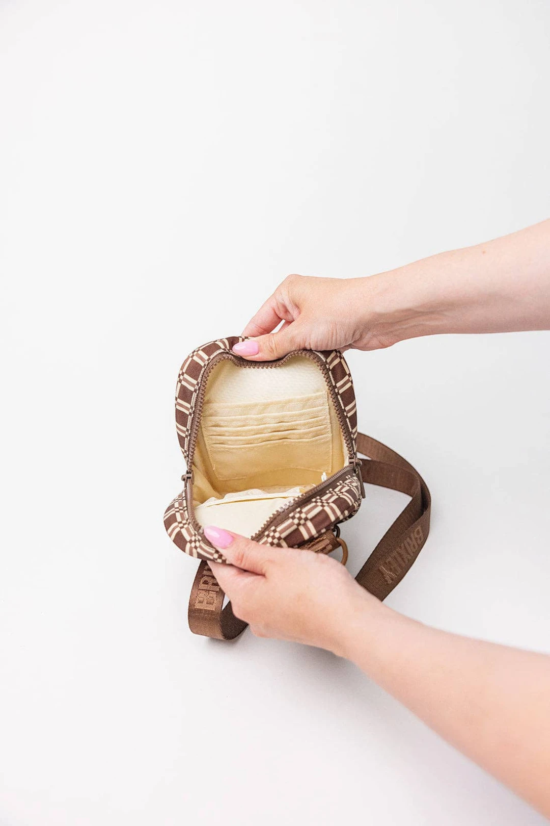 Person holding a small brown leather bag with intricate patterns on a white background