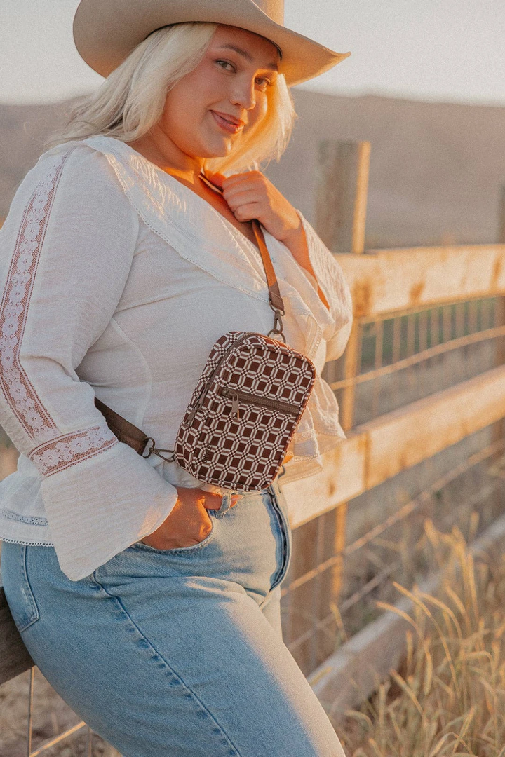 Woman wearing a beige hat and holding a patterned handbag, standing in a natural setting.