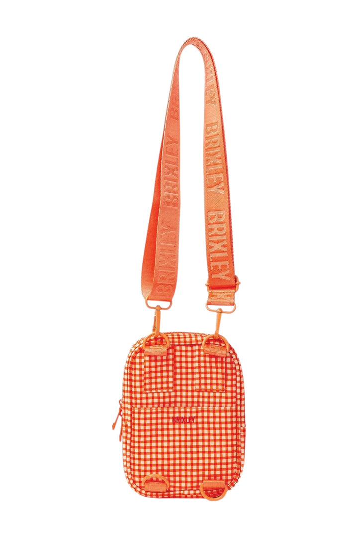 An orange and white gingham crossbody bag with a matching orange webbed strap featuring the brand name 'BRIXLEY' repeated, shown against a plain white background.