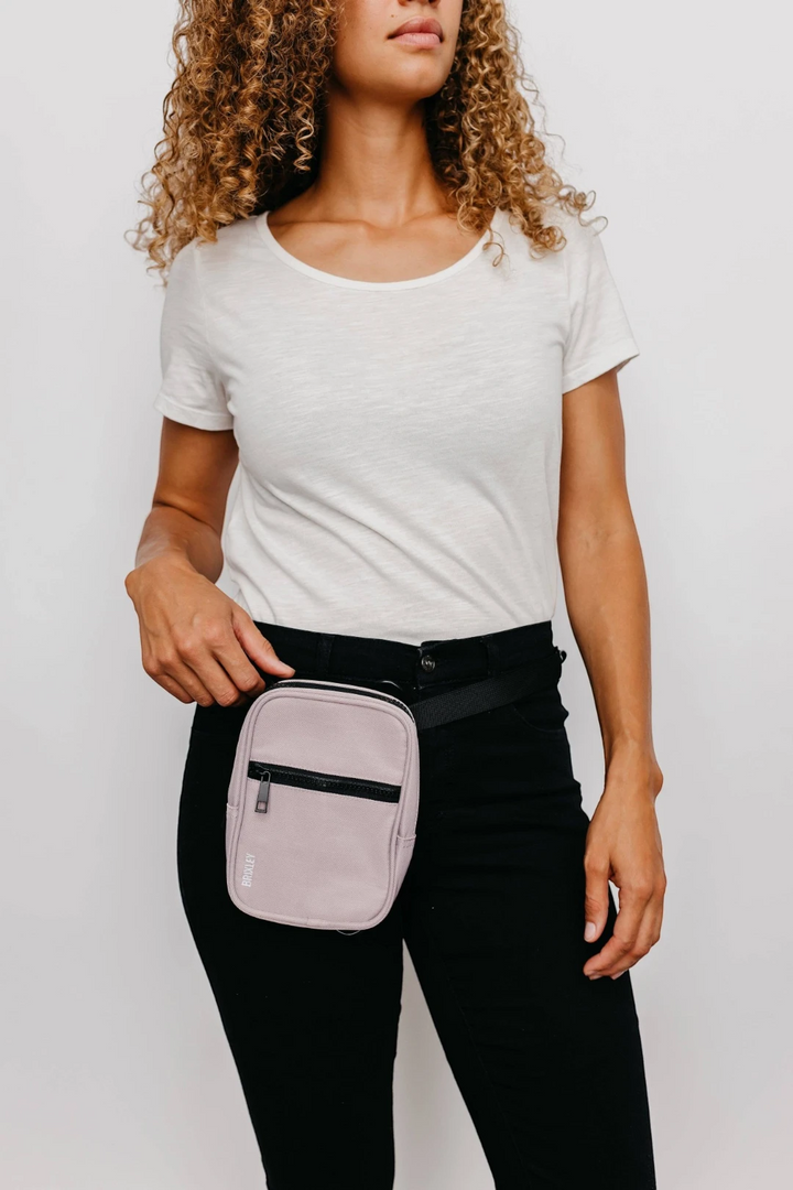 Person wearing a light pink waist bag on a plain background