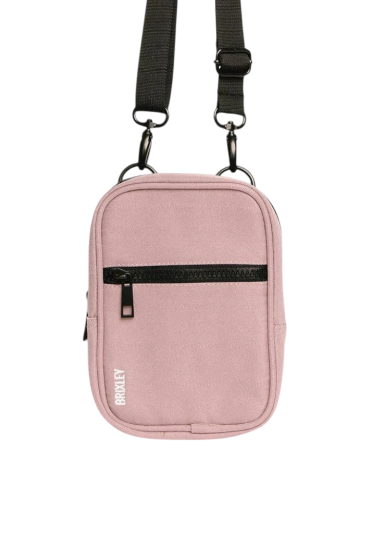 A dusty pink crossbody bag with a black adjustable strap and black zipper, featuring the brand name 'BRIXLEY' printed vertically in white on the lower left front.