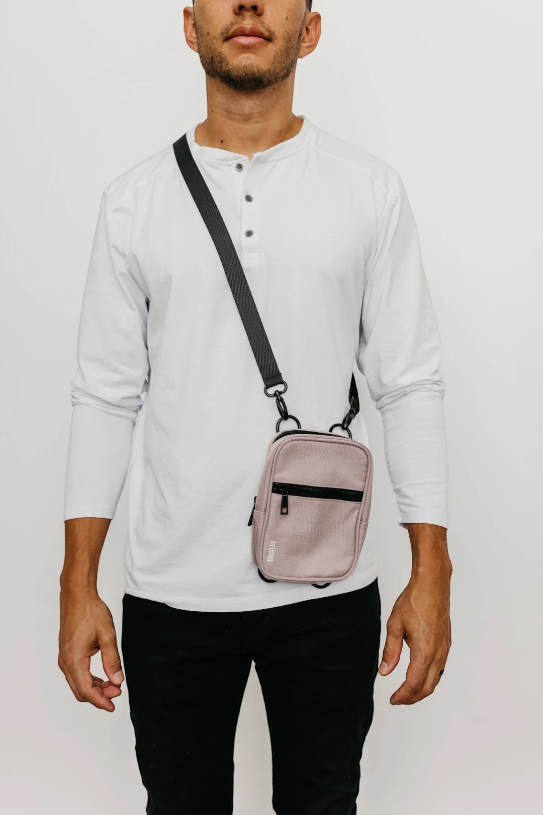 Person wearing a light gray long-sleeve shirt and black pants with a pink crossbody bag on a white background