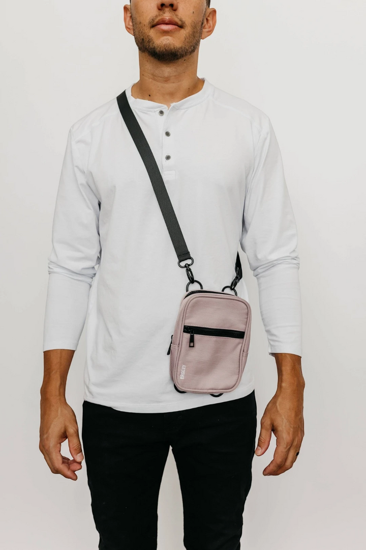 Person wearing a light gray long-sleeve shirt and black pants with a pink crossbody bag on a white background