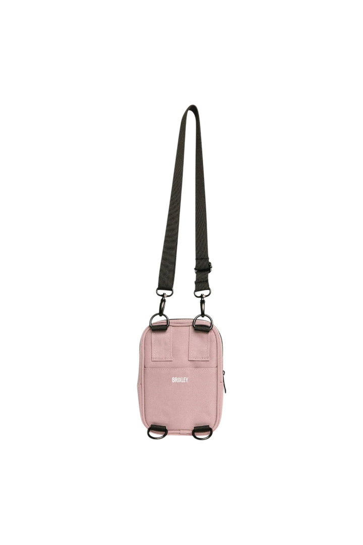 A light pink crossbody bag with a black adjustable shoulder strap and black hardware, featuring the brand name 'BRIXLEY' printed in white on the front.