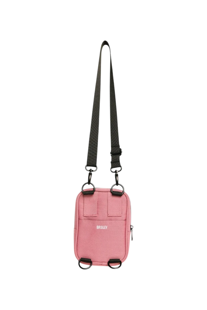 A pink crossbody phone bag with a black adjustable shoulder strap and black hardware, featuring the brand name 'BRIXLEY' printed in white on the front.