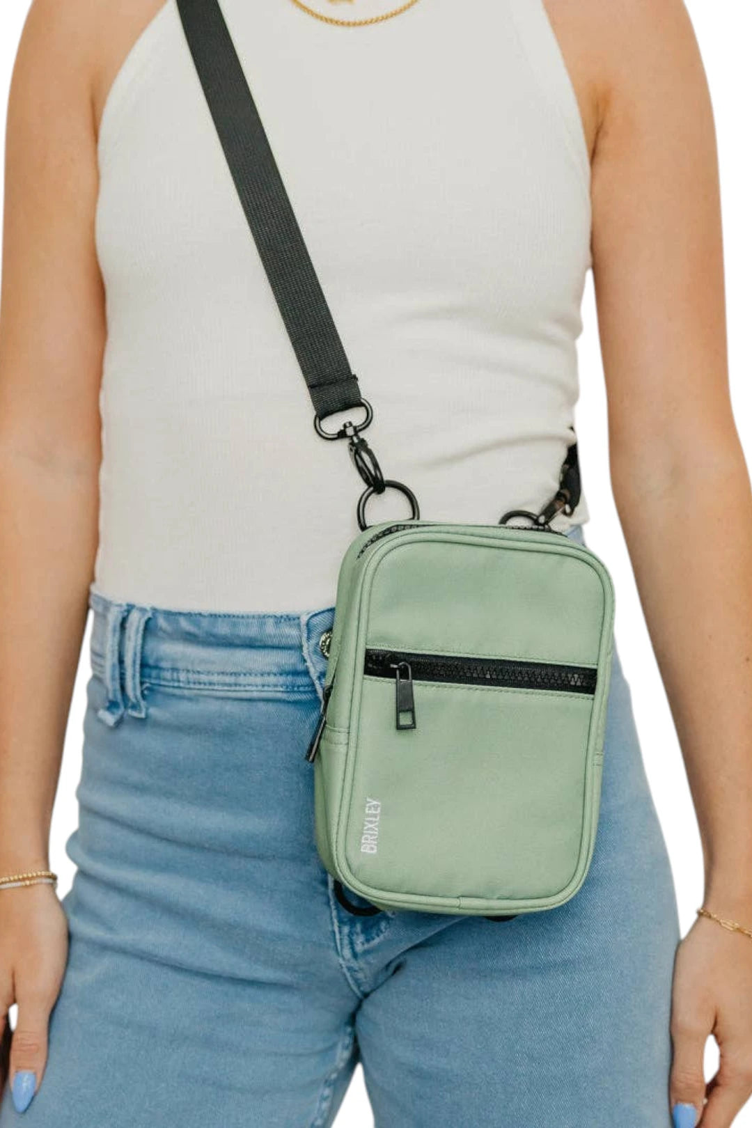 A mint green crossbody phone bag with a black strap and black zipper, worn by a model in a white tank top and blue jeans.