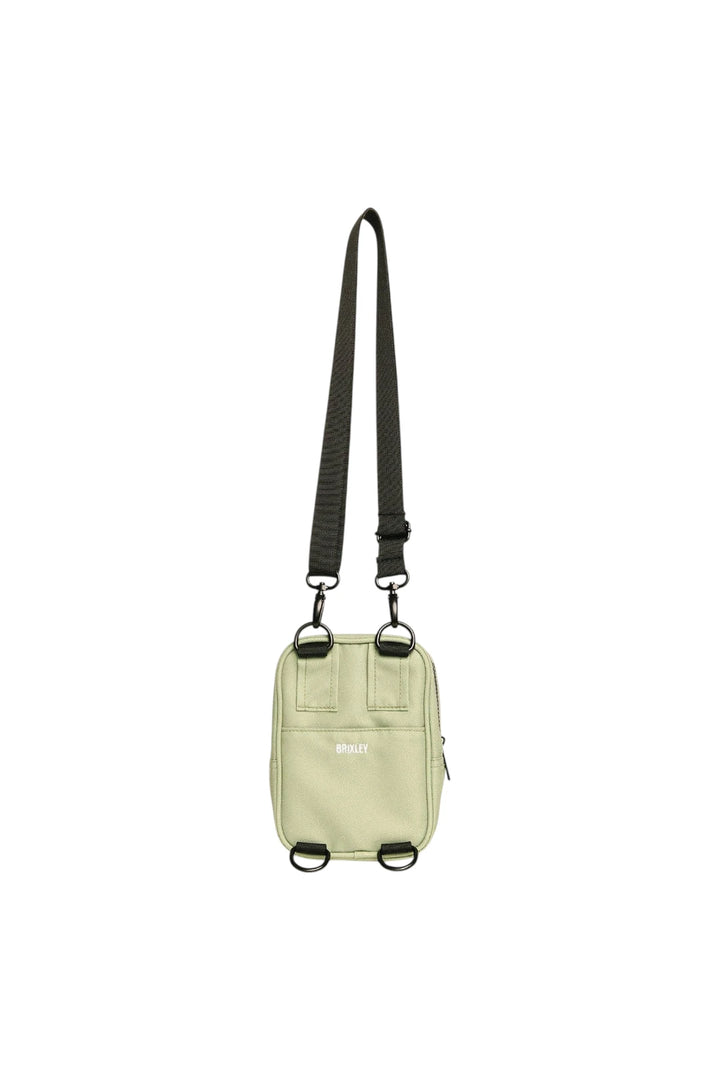 A small light sage green crossbody bag with a black adjustable shoulder strap and black metal hardware, shown against a plain white background.