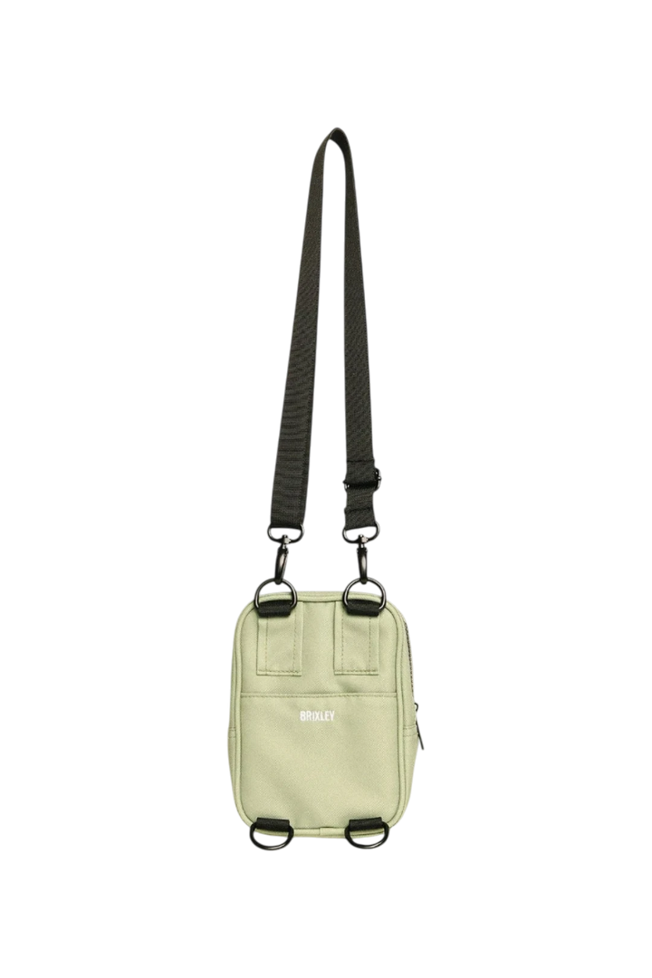 A light sage green utility pouch bag with a black adjustable shoulder strap, black metal hardware, and a small white logo on the front, shown against a plain white background.