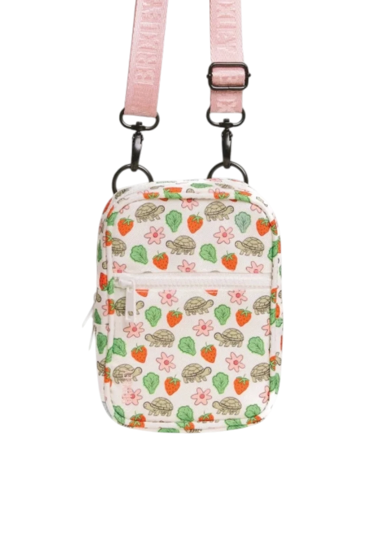 A small crossbody bag with a pink adjustable strap and a white body covered in a colorful pattern of sea turtles, strawberries, and leaves. The bag is shown against a plain white background.