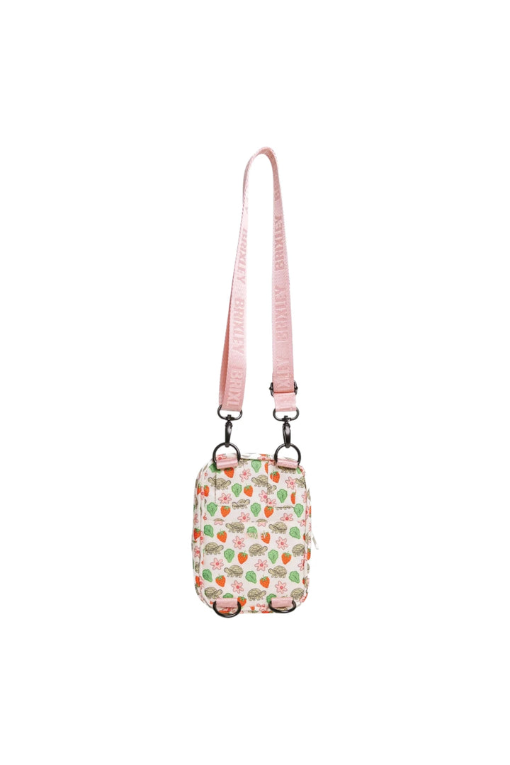 A small crossbody bag with a pink strap and a white body covered in a colorful pattern of turtles, strawberries, and lettuce shown against a plain white background.