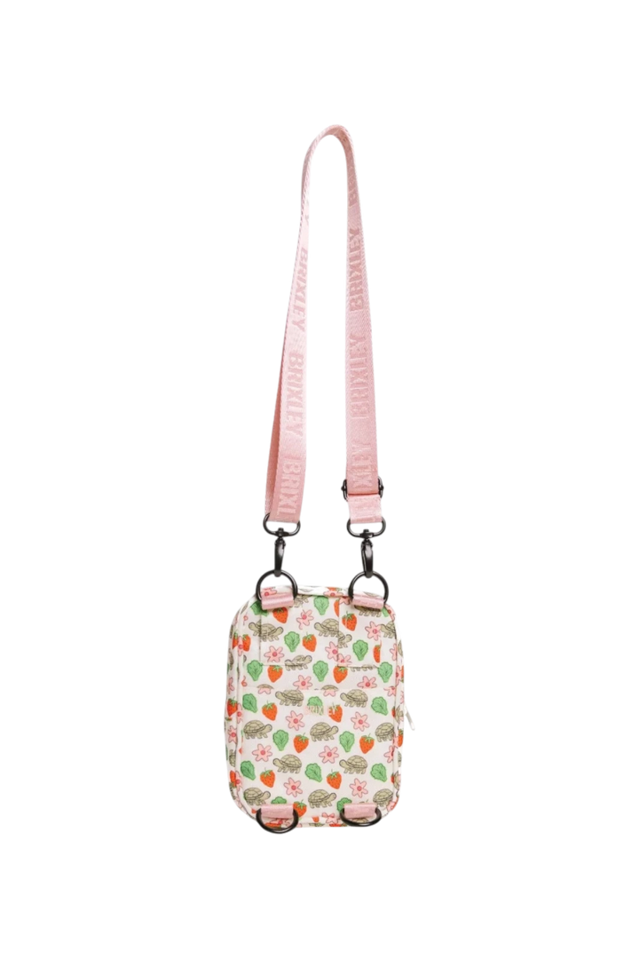 A small crossbody bag with a pink strap and a white body covered in a strawberry and green leaf pattern, shown against a plain white background.
