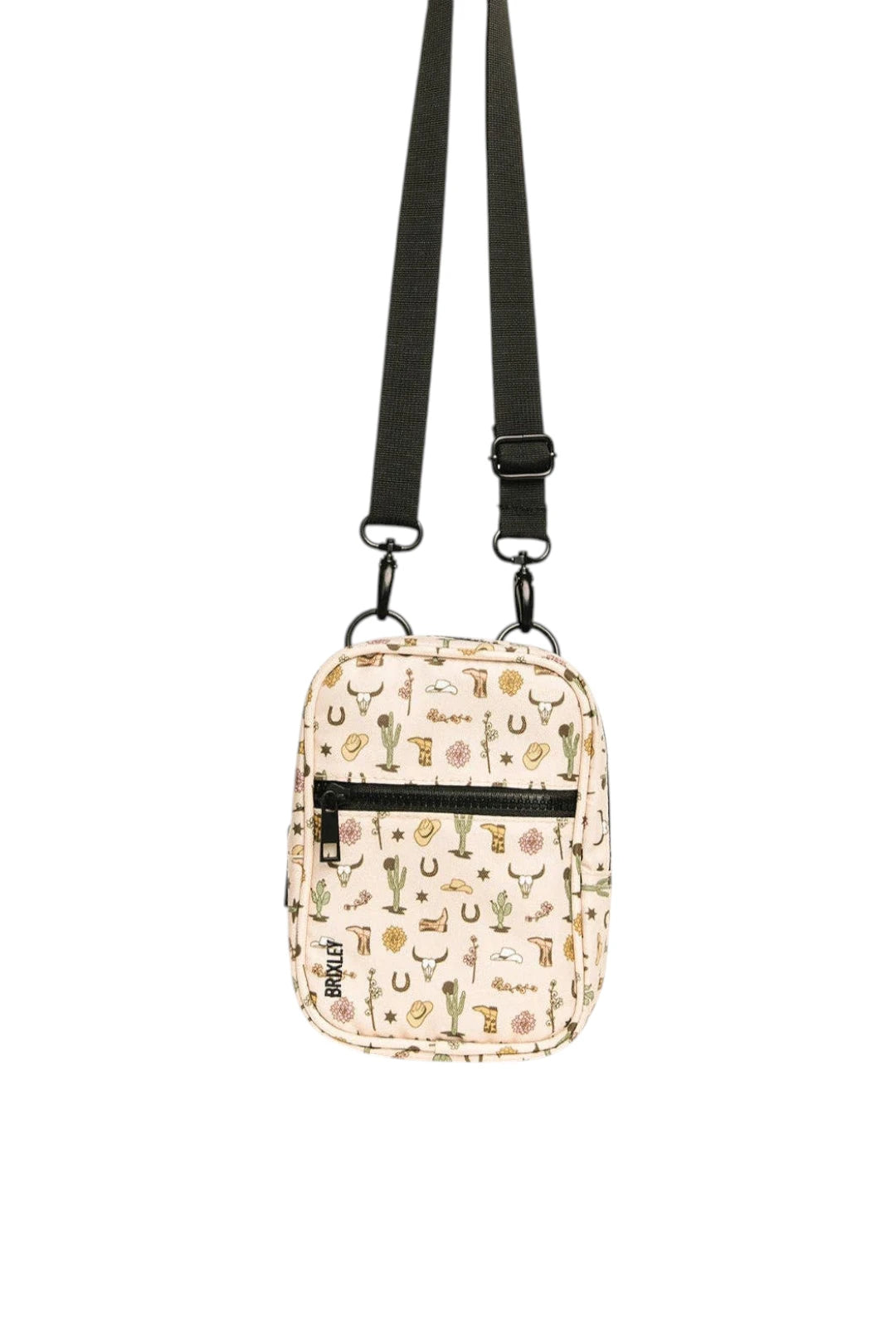 A small crossbody bag with a beige background and a colorful pattern of cacti, horseshoes, and western-themed illustrations. It features a black adjustable shoulder strap, a black front zipper pocket, and a black vertical brand tag that reads 'trtl'.