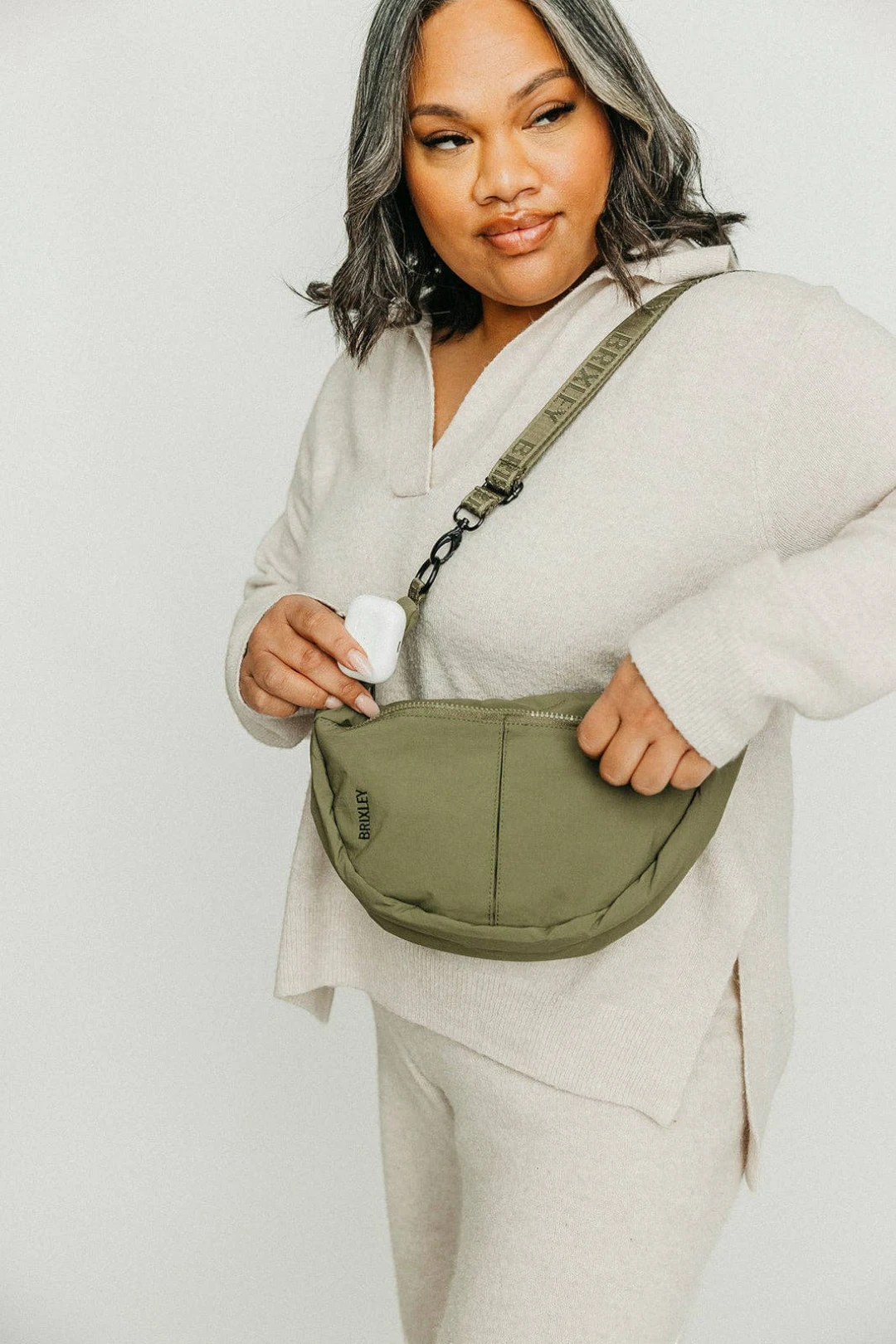Woman holding a green crescent bag against a plain background
