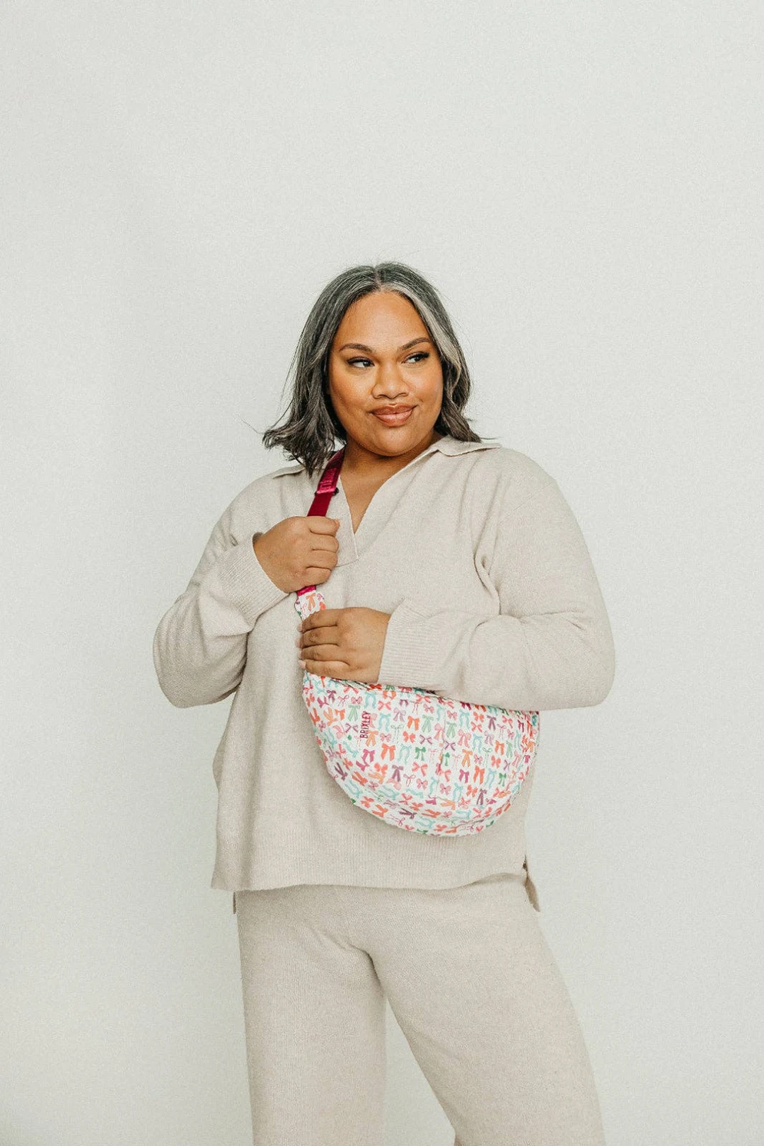 Woman wearing a beige outfit with a colorful patterned bag on a plain background
