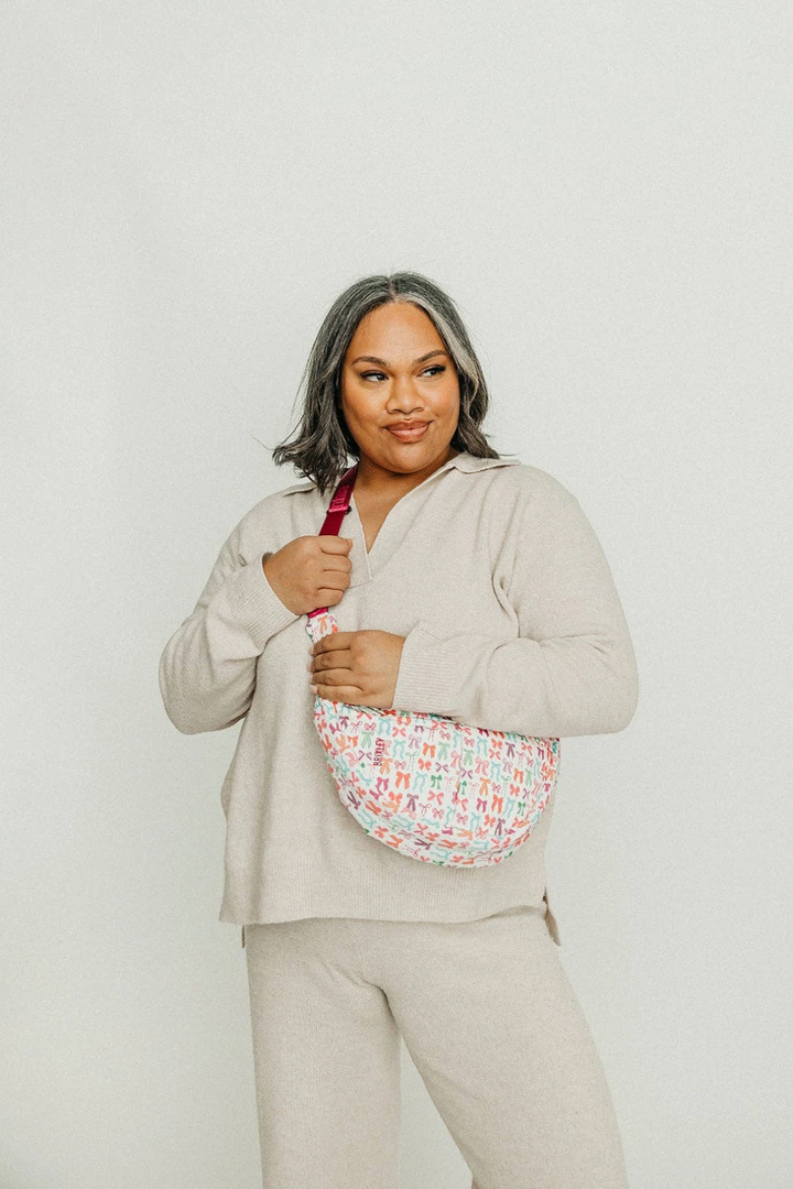Woman wearing a beige outfit with a colorful patterned bag on a plain background