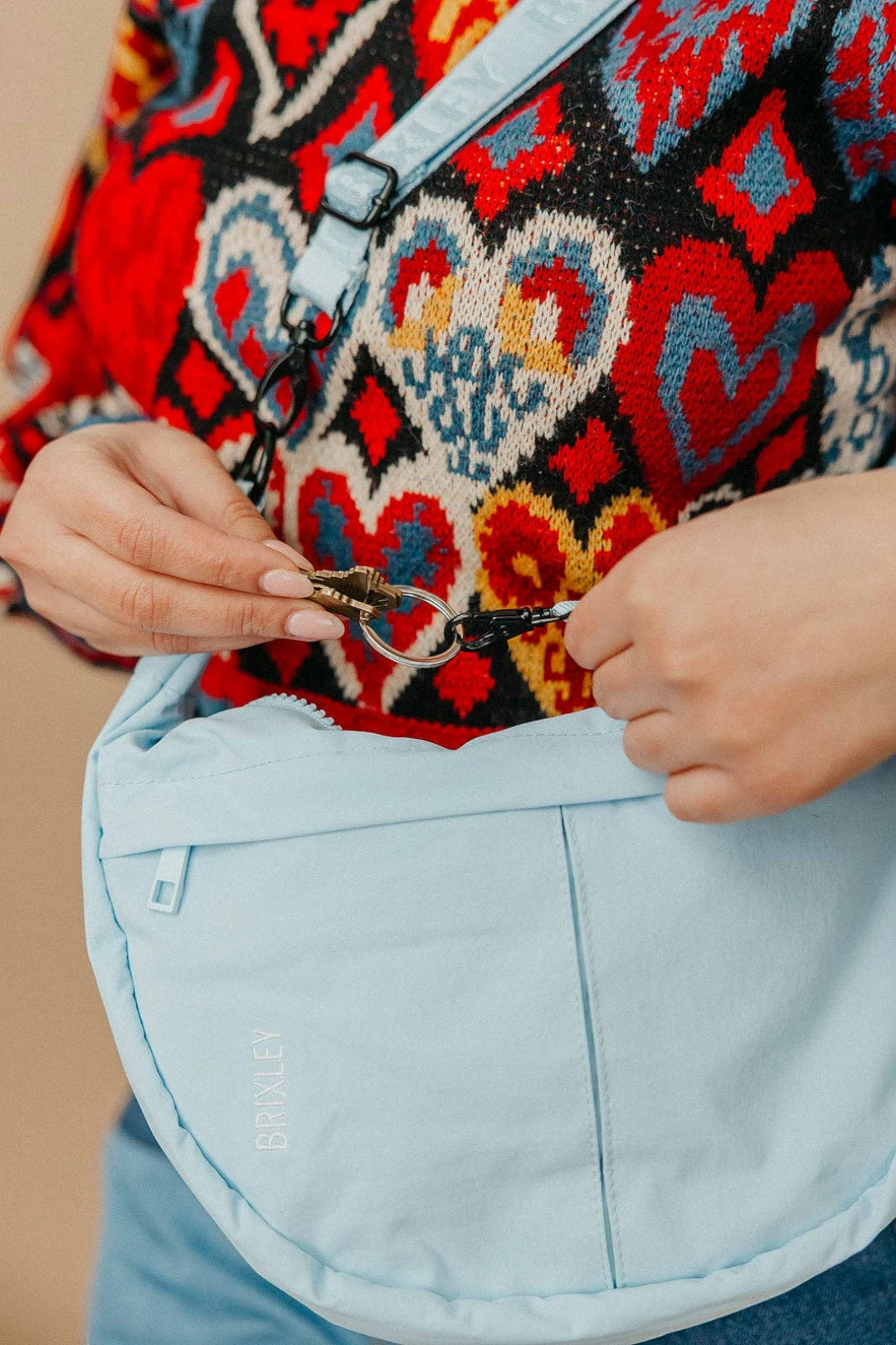 Person wearing a colorful patterned garment with a focus on a crescent bag and light blue pants.