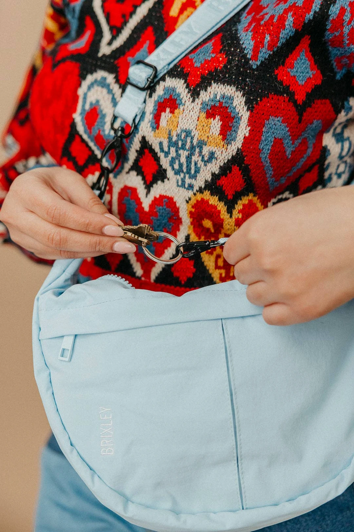 Person wearing a colorful patterned garment with a focus on a crescent bag and light blue pants.