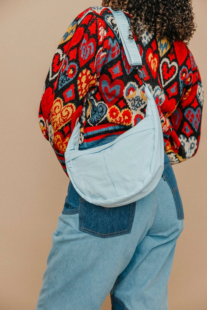 Person wearing a colorful patterned crescent bag with a light blue strap on a beige background