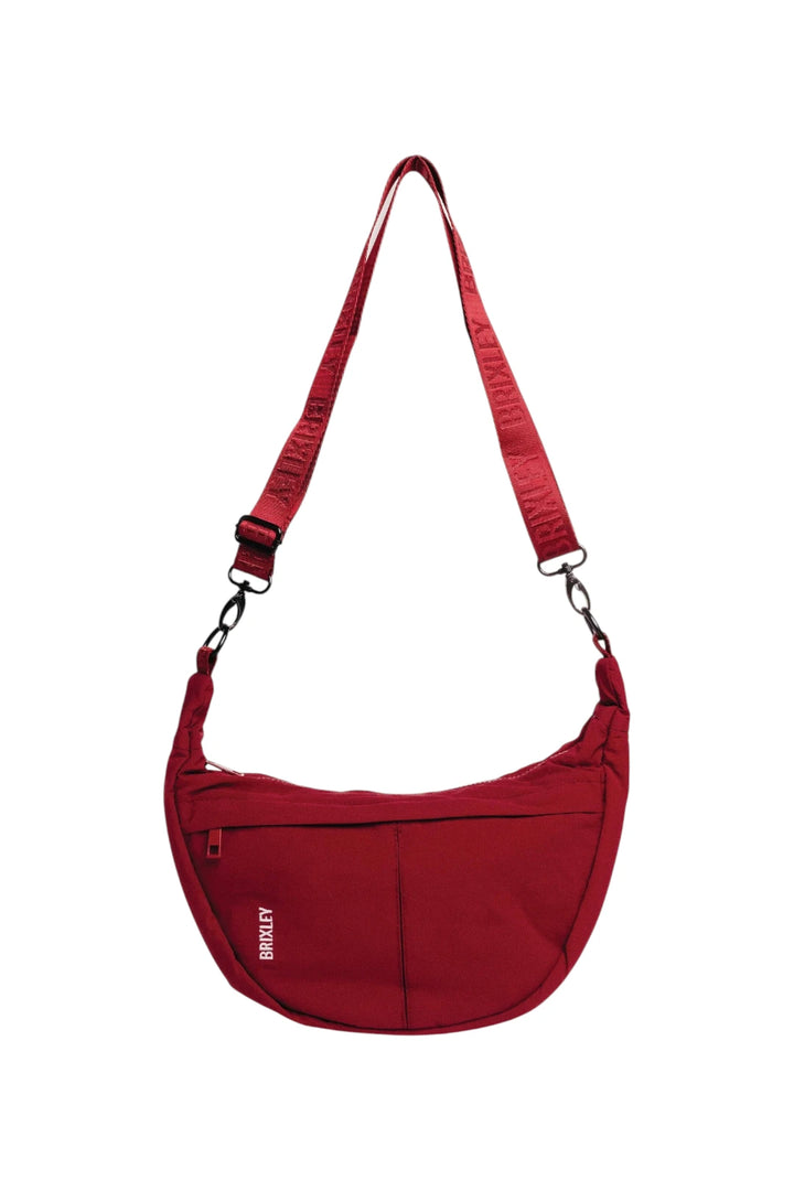 A red crescent-shaped shoulder bag with an adjustable shoulder strap and a front zippered pocket, shown against a plain white background.