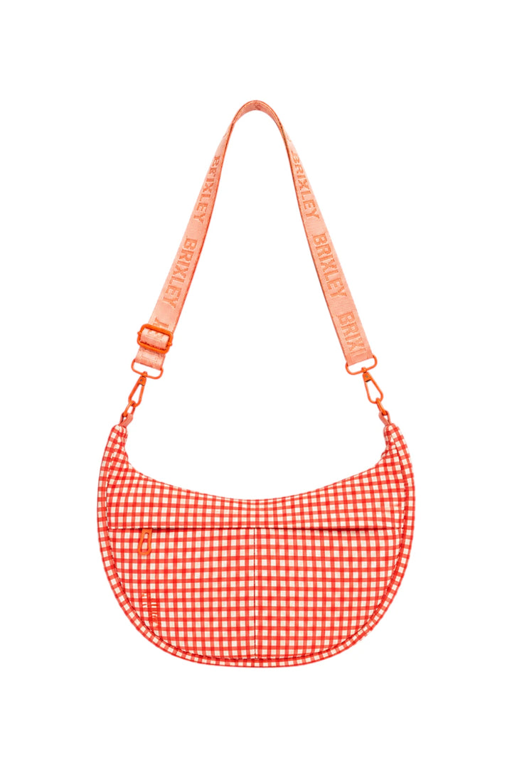 A crescent-shaped shoulder bag with a red and white gingham pattern, featuring a matching red and white gingham strap with the brand name 'BRIXLEY' printed repeatedly, set against a plain white background.