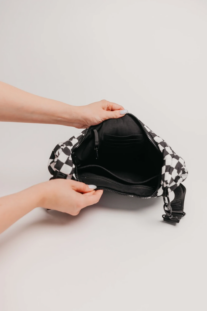 A black and white checkered shoulder bag with a black interior, shown being held open by two hands against a light gray background.
