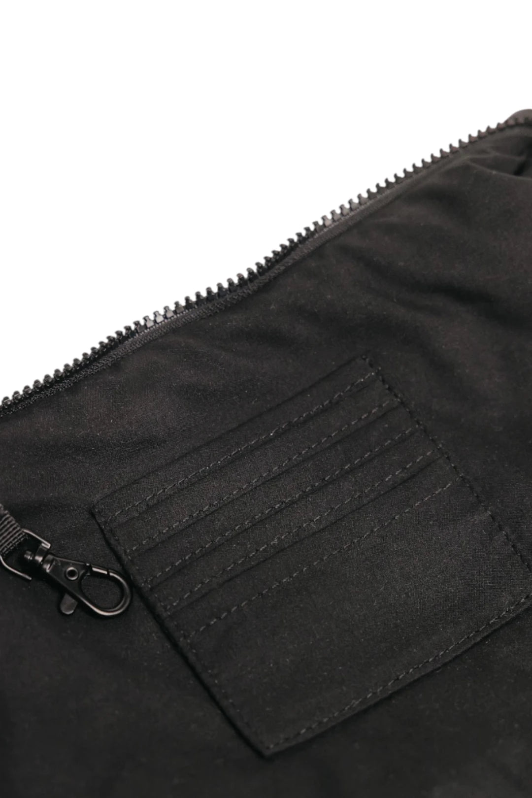 Close-up of a black fabric zippered pouch or bag showing a stitched pocket detail and metal clasp on a white background.