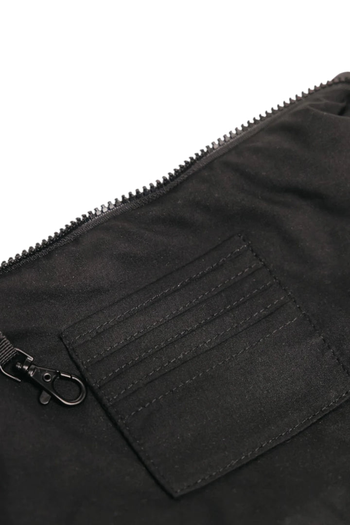 Close-up of a black fabric zippered pouch or bag showing a stitched pocket detail and metal clasp on a white background.