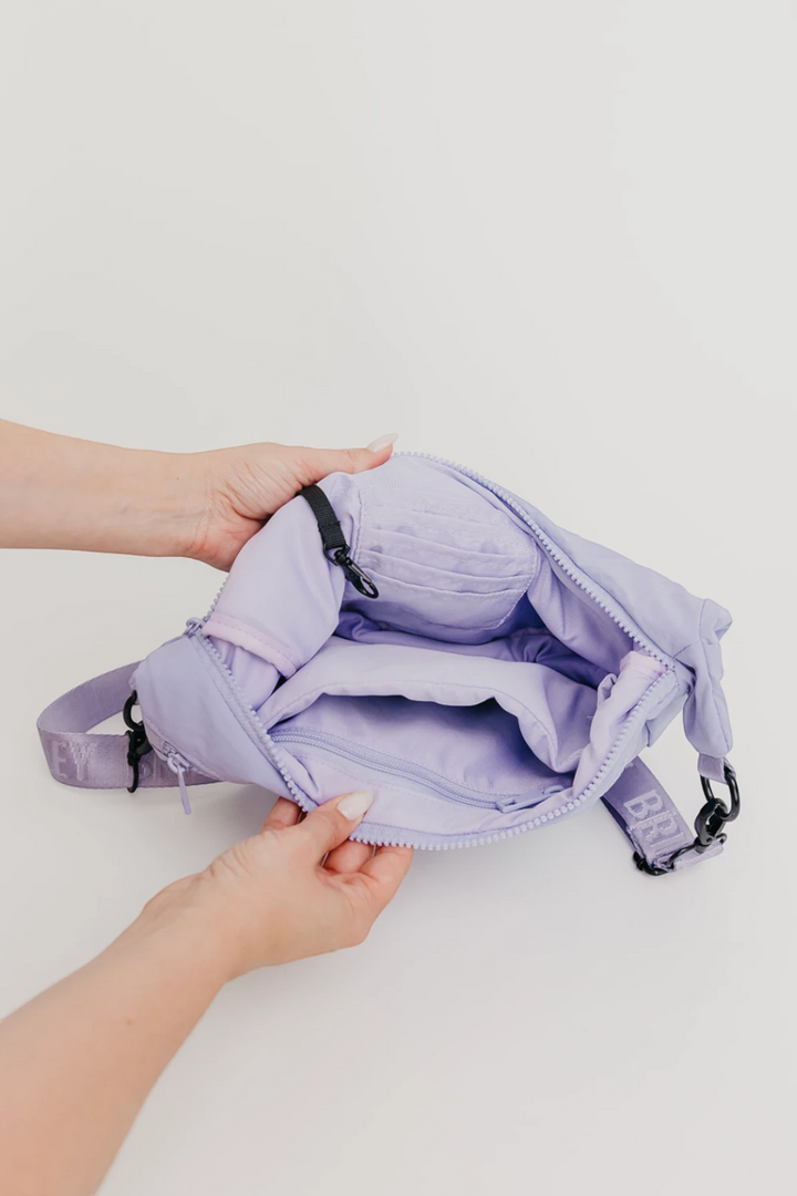 A lavender purple crossbody bag with black hardware, held open by two hands against a clean white background.