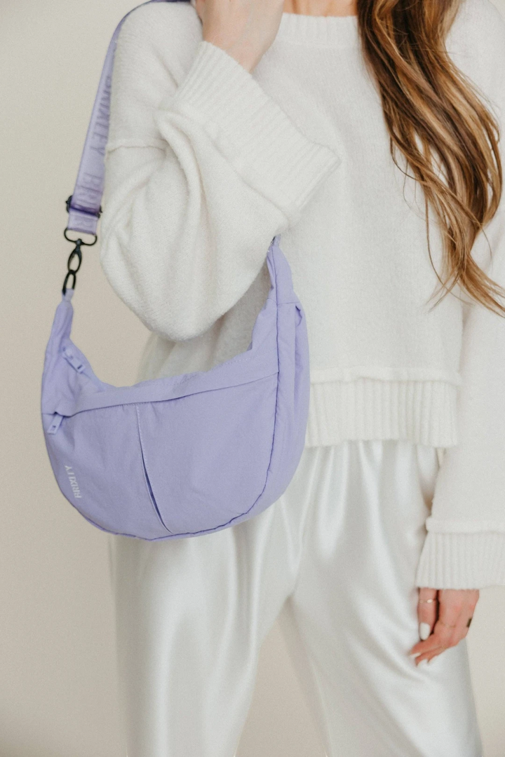 Person holding a purple shoulder bag against a neutral background
