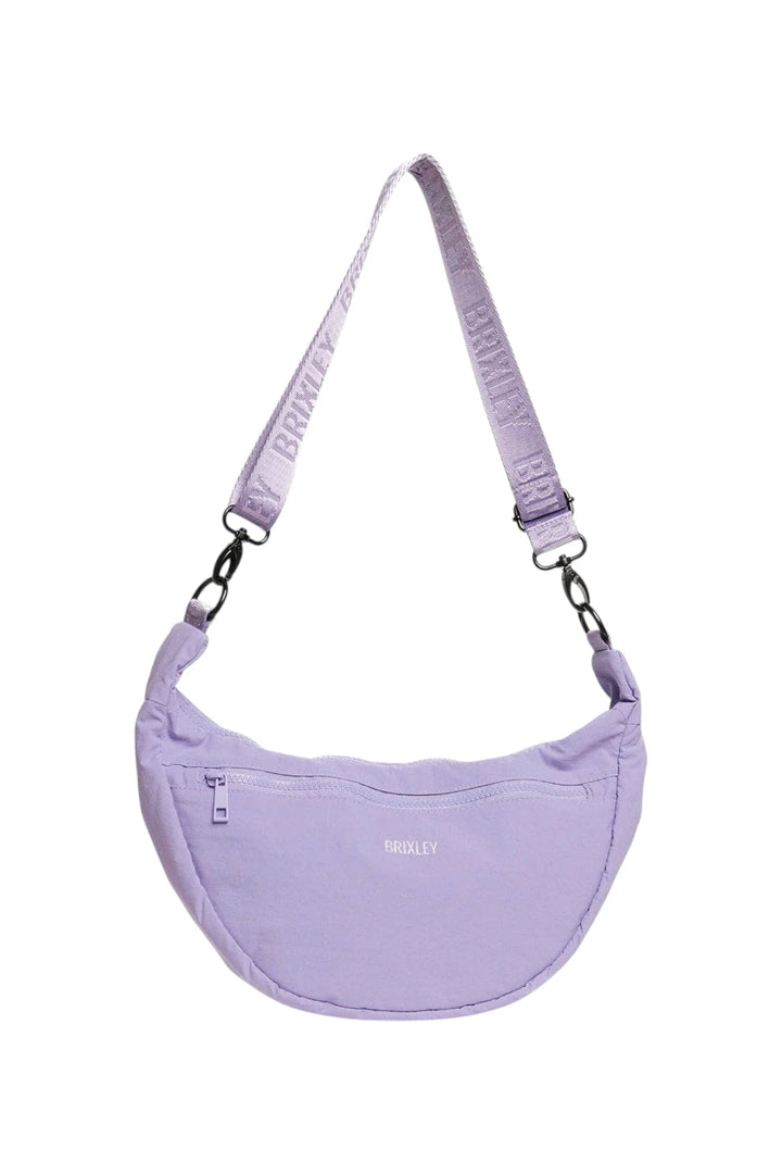 A light purple crescent-shaped shoulder bag with a matching adjustable strap featuring the brand name 'BRIXLEY' printed repeatedly. The bag has a small front zip pocket and a subtle BRIXLEY logo on the front, set against a plain white background.
