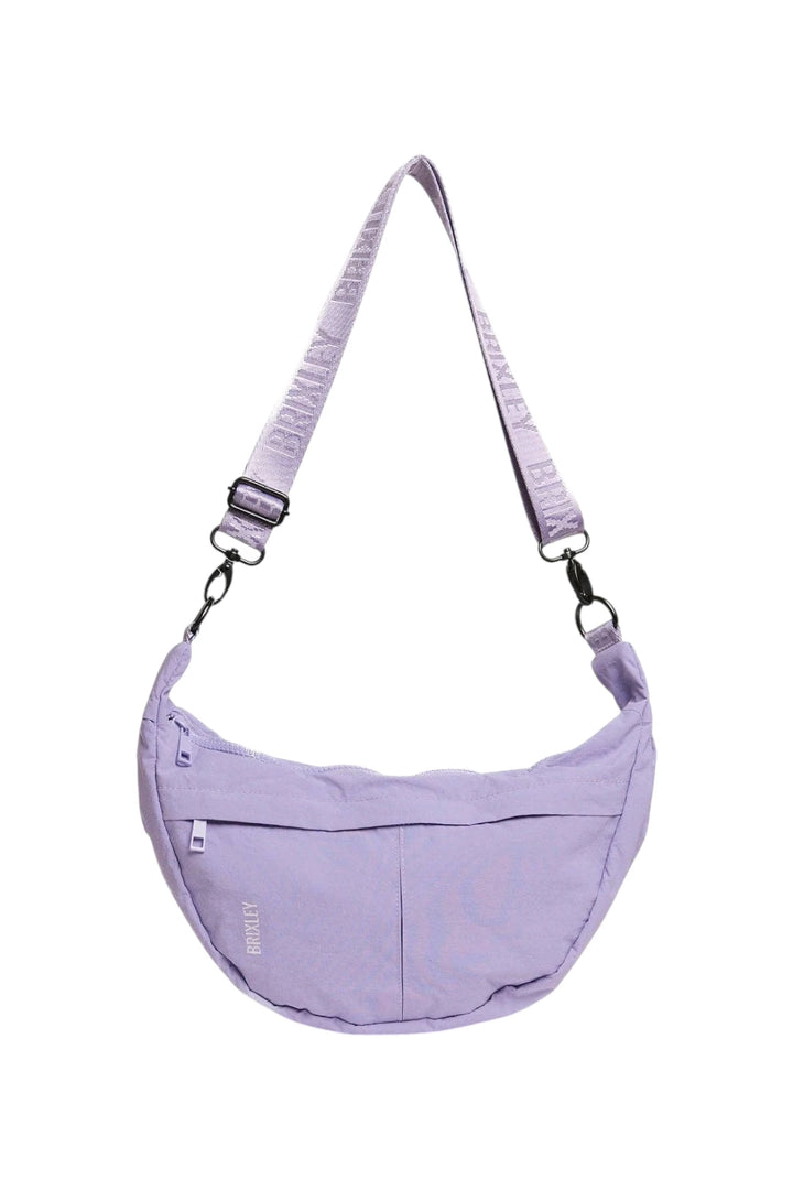 A light purple crescent-shaped shoulder bag with an adjustable, zippered strap, featuring a front zip pocket and a small vertical 'BRIXLEY' brand label, shown against a plain white background.