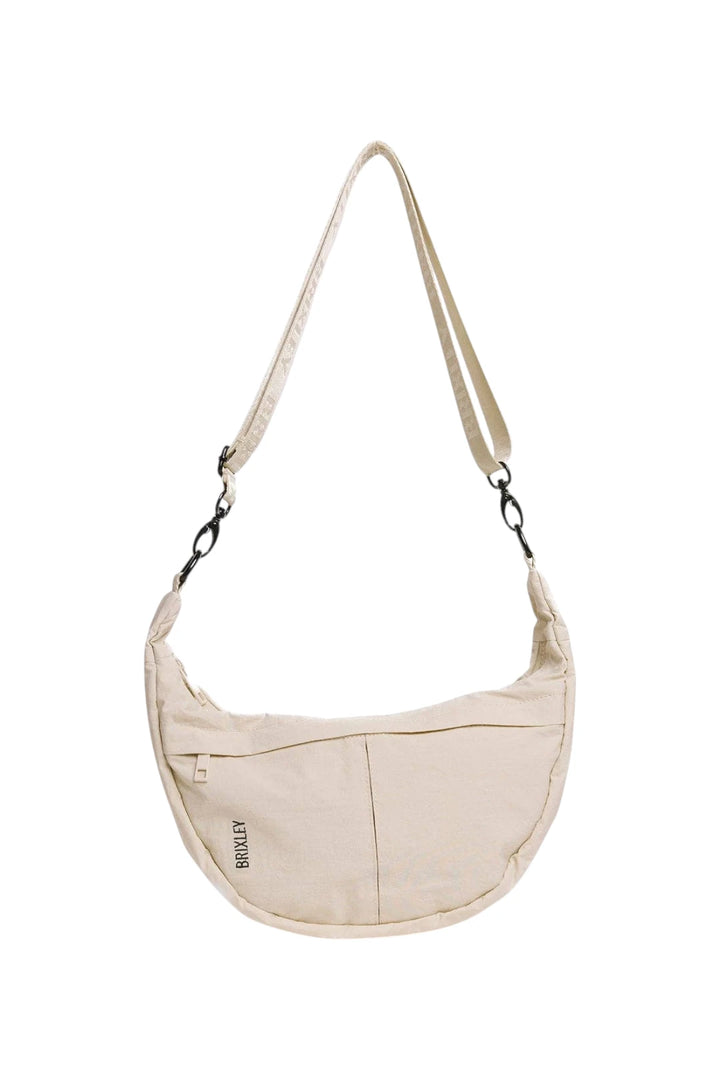 A cream-colored canvas crescent shoulder bag with a matching adjustable shoulder strap and black metal hardware, shown against a plain white background.