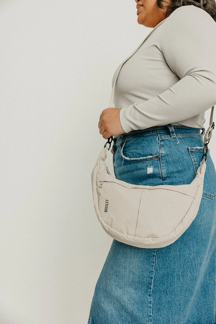 Person wearing a beige crossbody bag with a plain background