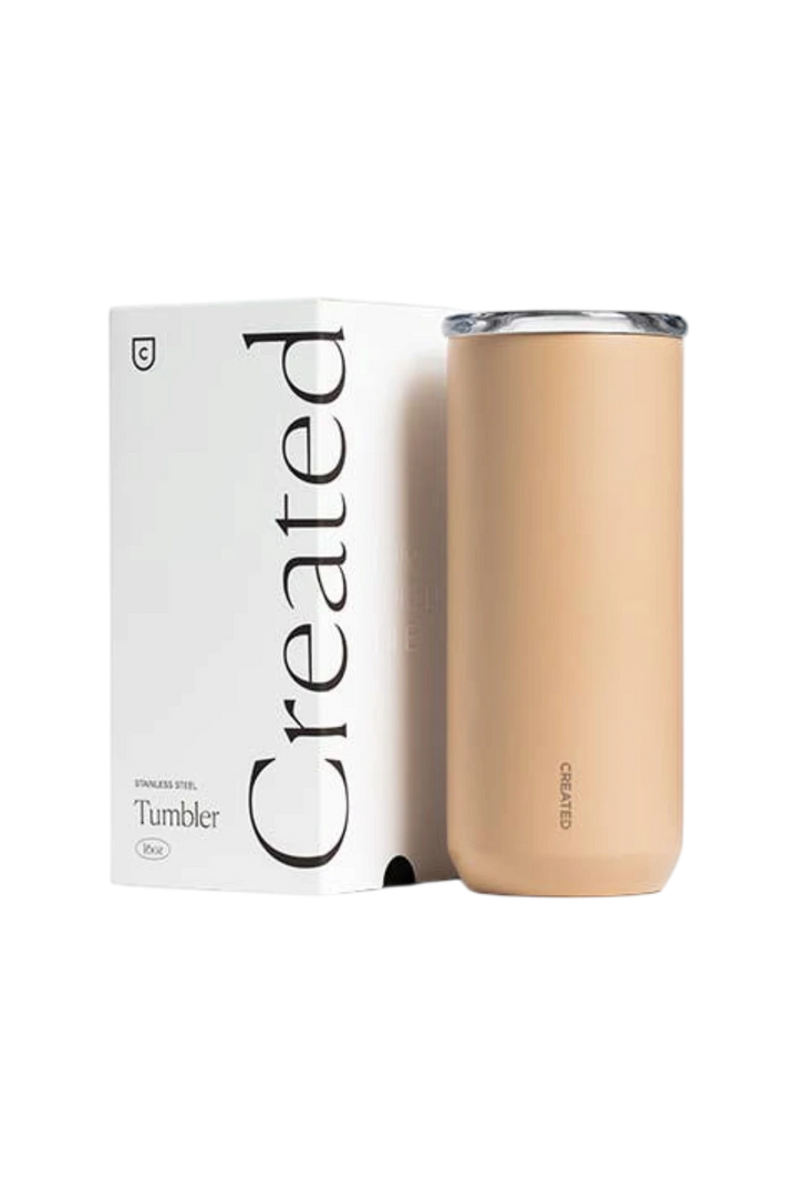 A beige insulated stainless steel tumbler with a clear lid stands next to its white packaging box, which features the brand name 'Created' in large black lettering.